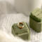 14K yellow gold birthstone stackable rings with 2mm round stones on a green velvet box, white fabric, and green plant in the background.
